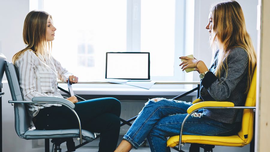 Vue de profil de deux jeunes femmes lors d'un entretien devant un bureau.